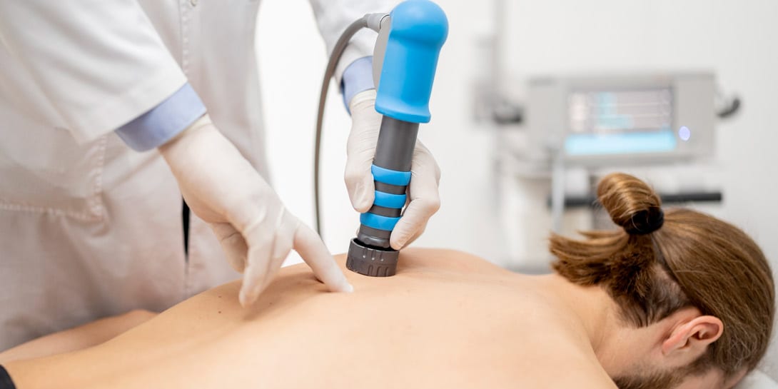 Doctor applies shock wave therapy with special medical equipment on men's back at medical office, close-up view. Concept of non-invasive technology for treating pain in the musculoskeletal system