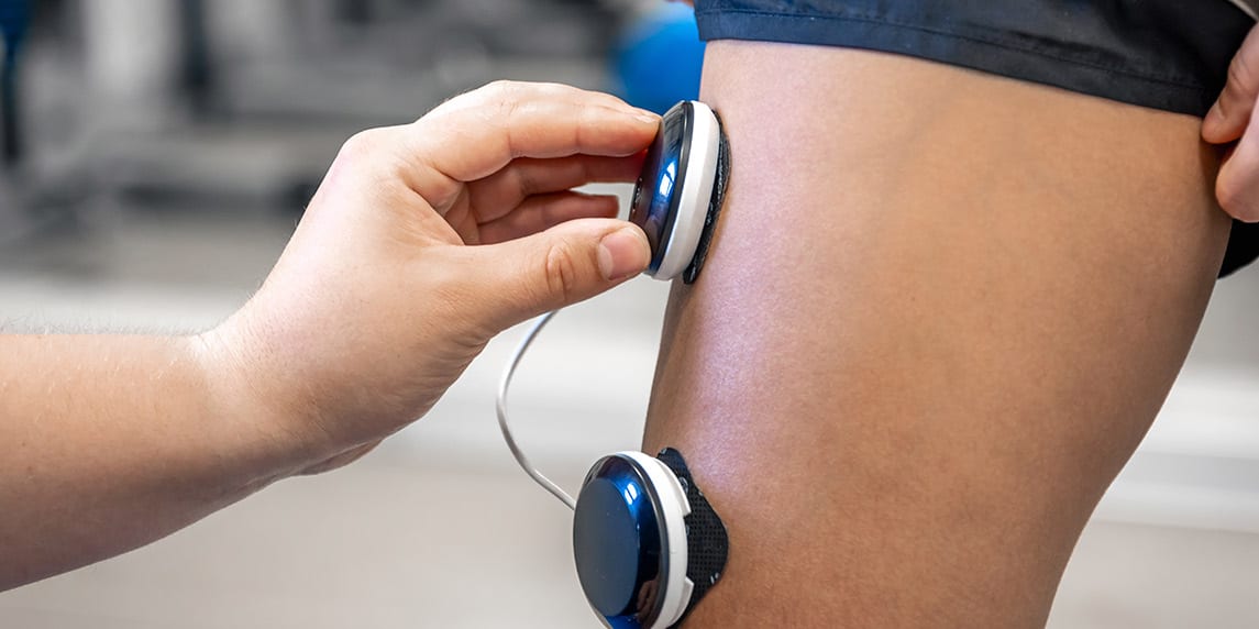 Individual using an electronic device to measure their leg, highlighting the advantages of PEMF therapy.