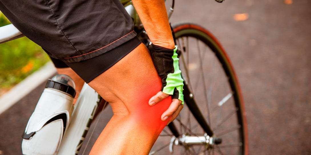 Senior Woman cyclist holding hand on knee in pain, massaging her gliding joint bone. Arthritis cramp in the knee while cycling outdoor. Painful spot highlight in red. Copy space