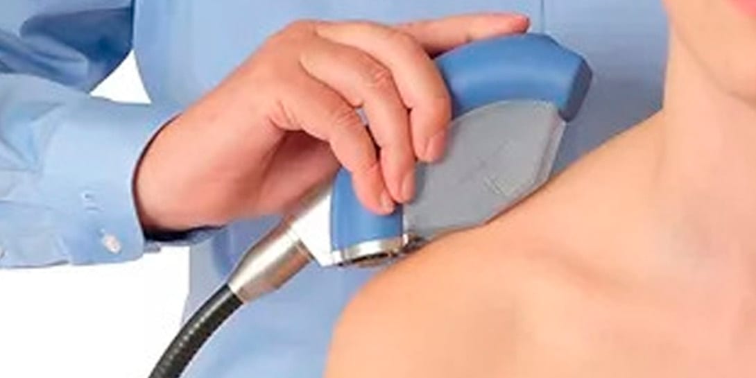 Doctor applies shock wave therapy with special medical equipment on men's back at medical office, close-up view. Concept of non-invasive technology for treating pain in the musculoskeletal system