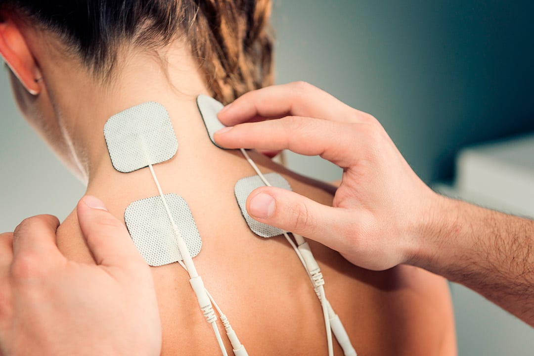 A woman demonstrates PEMF therapy by holding a device on her back, showcasing its healing benefits.