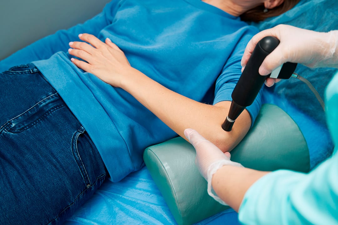 A woman receives a shockwave treatment in her arm during a medical procedure.