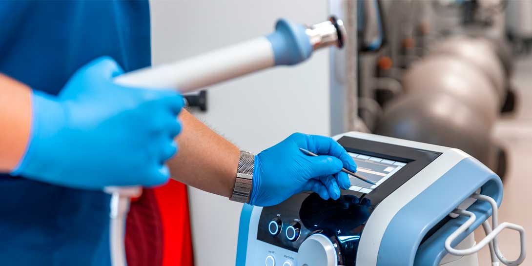 Shock wave therapy device with male doctor hands in rubber gloves.